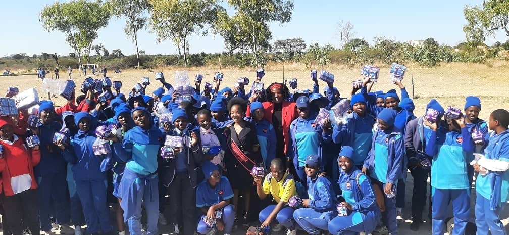 Large group of people wearing blue shirts and caps celebrating together outdoors in a dry, grassy field with scattered trees