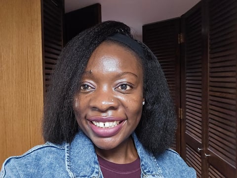 Smiling woman with long black hair wearing a denim jacket and maroon top, photographed indoors with wooden doors in background