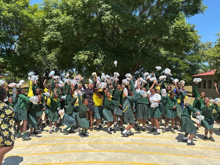 Group of schoolchildren in green uniforms holding white papers, standing together outdoors under large trees